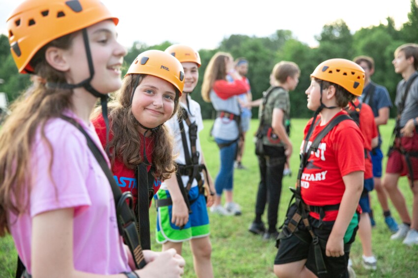 Girl smiling in group of kids in ziplining gear.