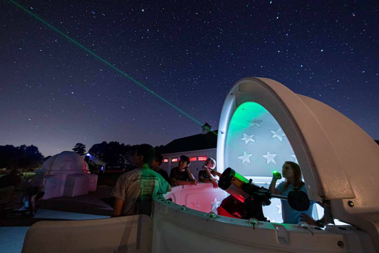 Telescope with girl flashing green light night sky.