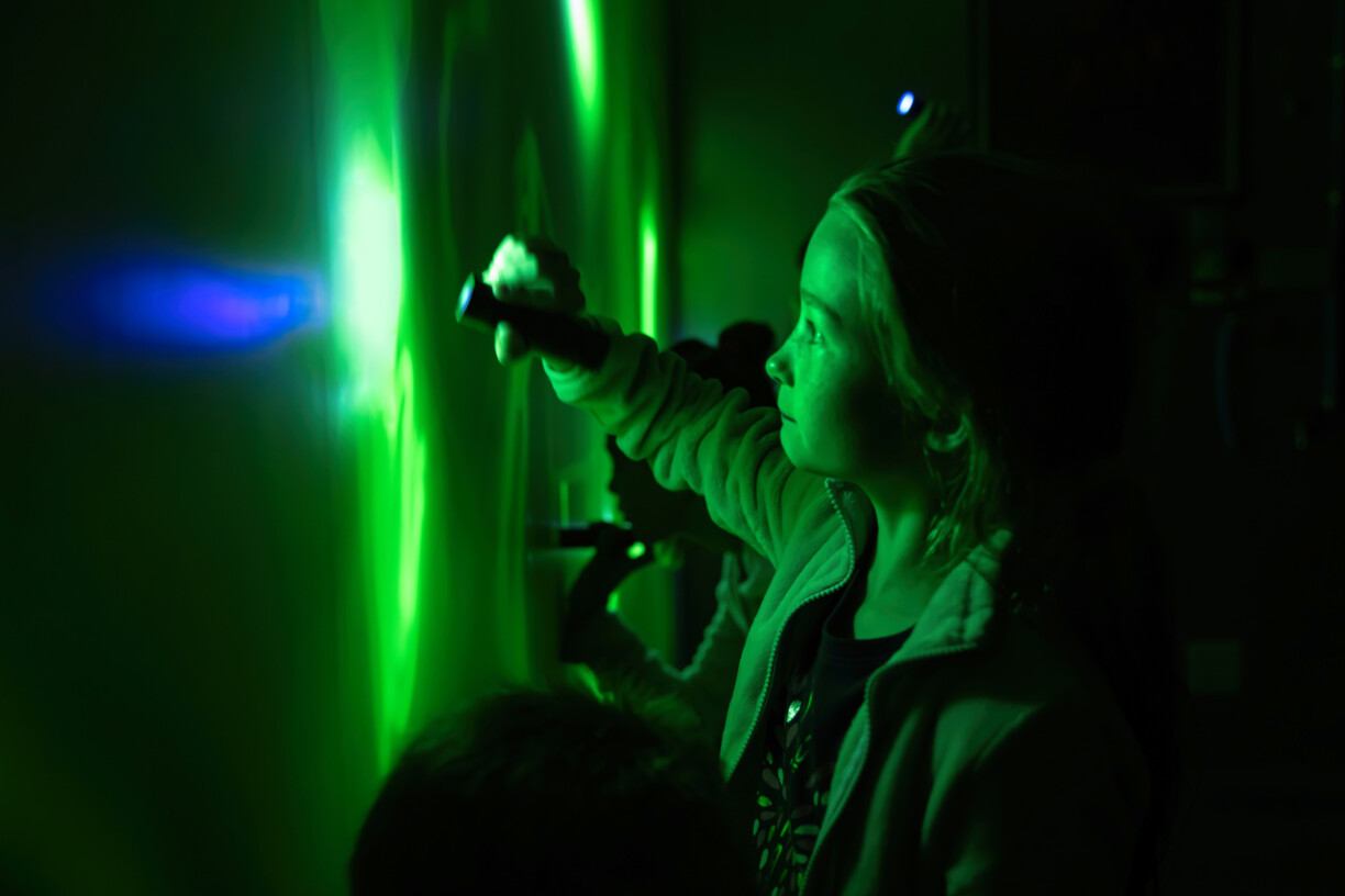 Girl using flashlight on green wall.