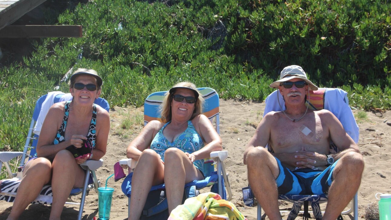 Three people smiling at beach reunion.